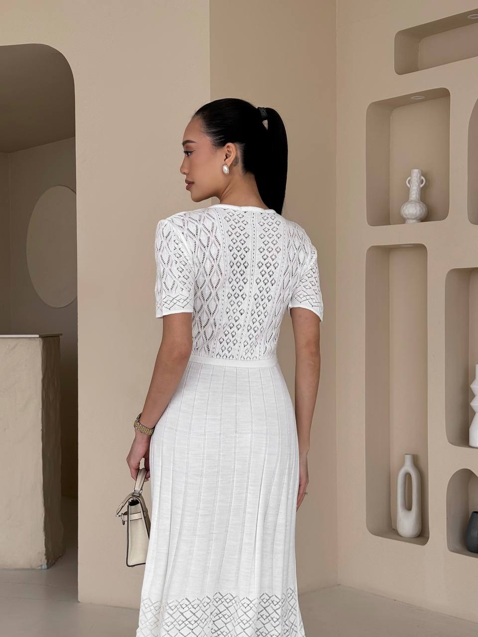 Woman in a white lace dress standing in a minimalistic room with geometric wall designs.
