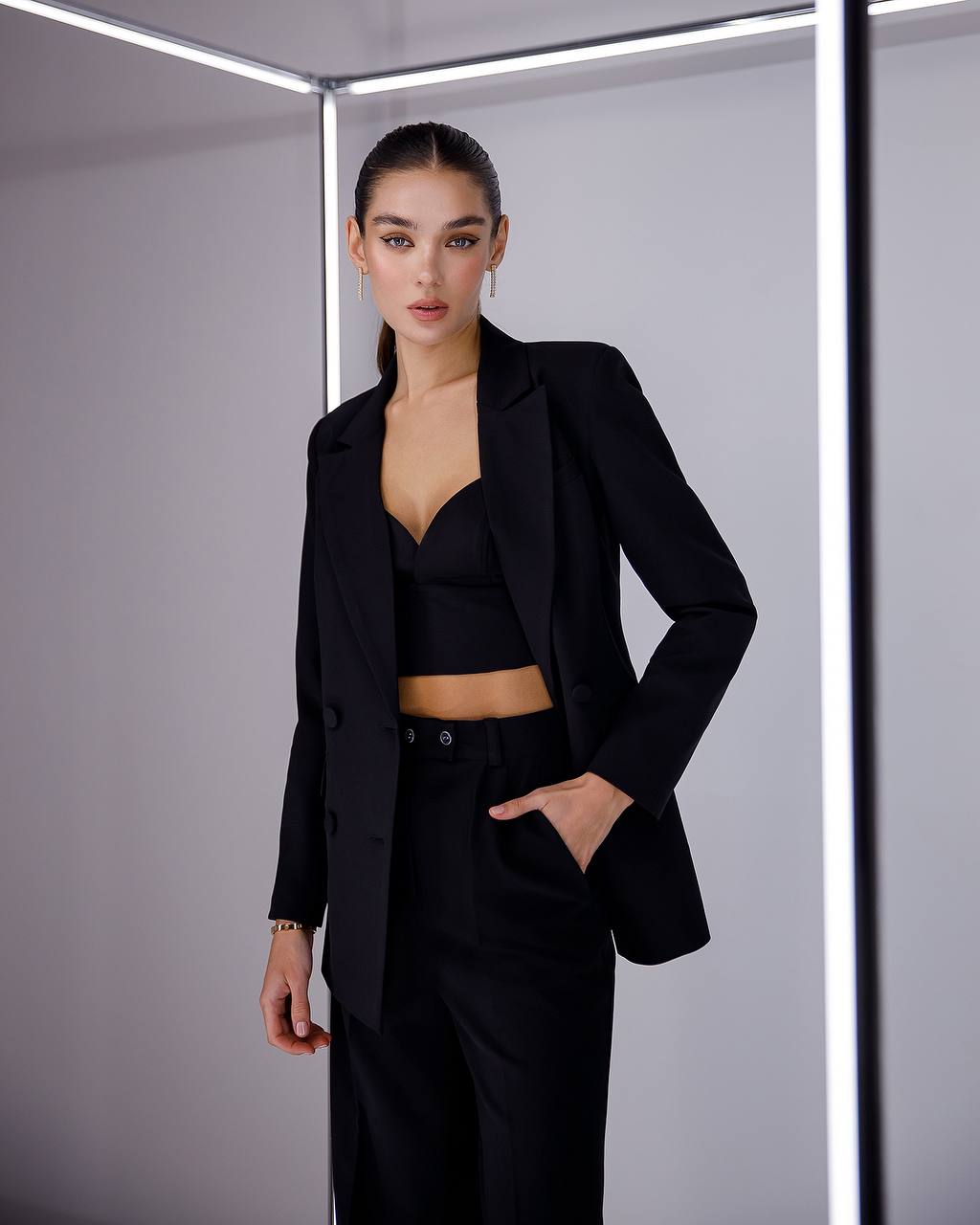 Woman wearing a black suit standing against a neutral background