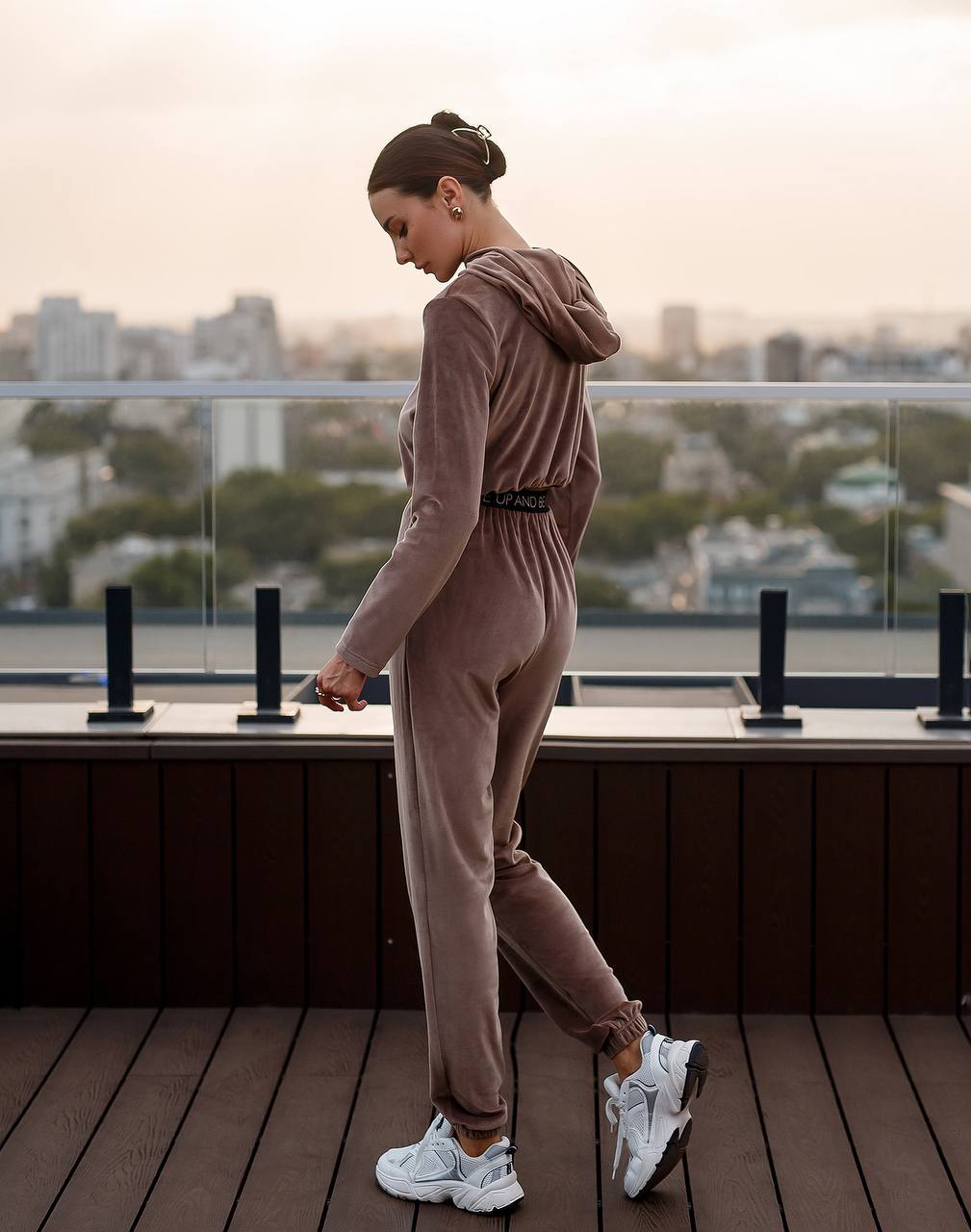 Woman in a pink tracksuit standing on a rooftop with a cityscape in the background