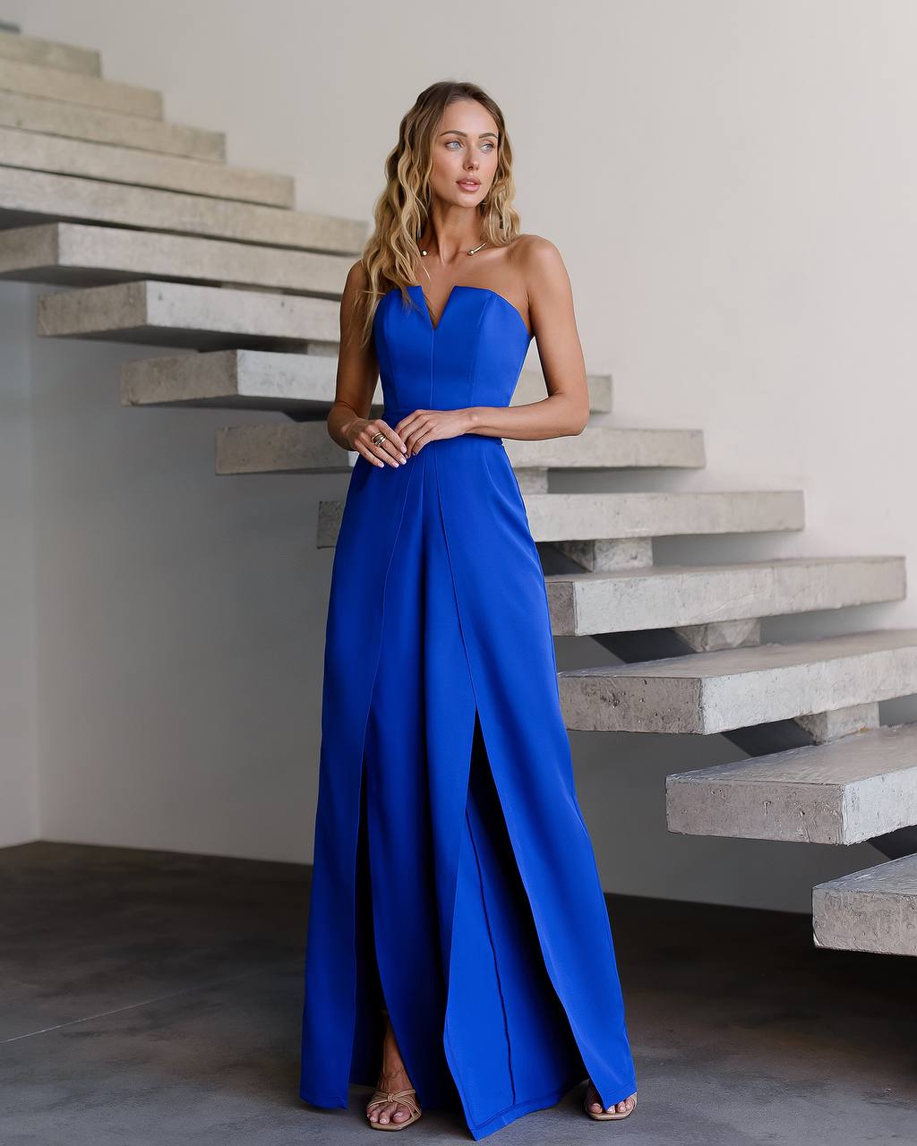Woman in a blue strapless gown standing in front of concrete stairs.