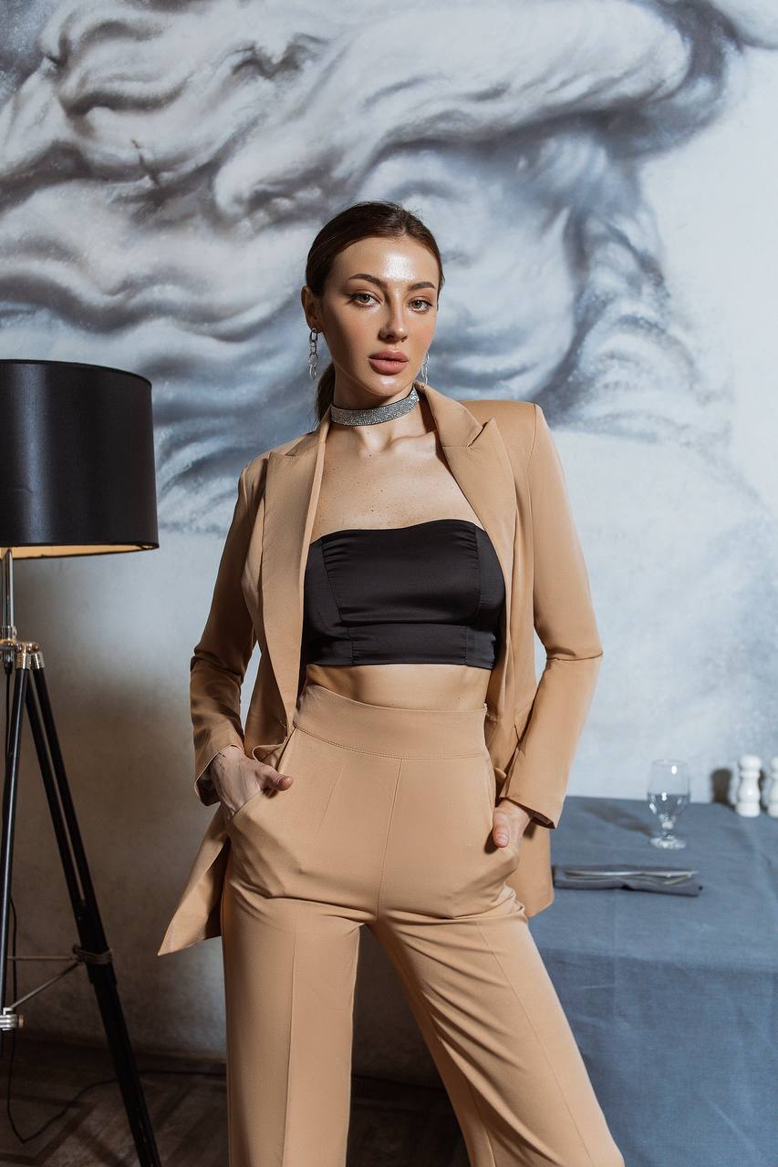 Woman in a beige suit standing in a room with a marble wall and table setting.