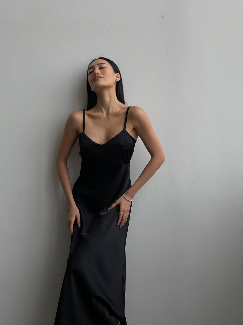 Woman wearing a black slip dress against a plain background