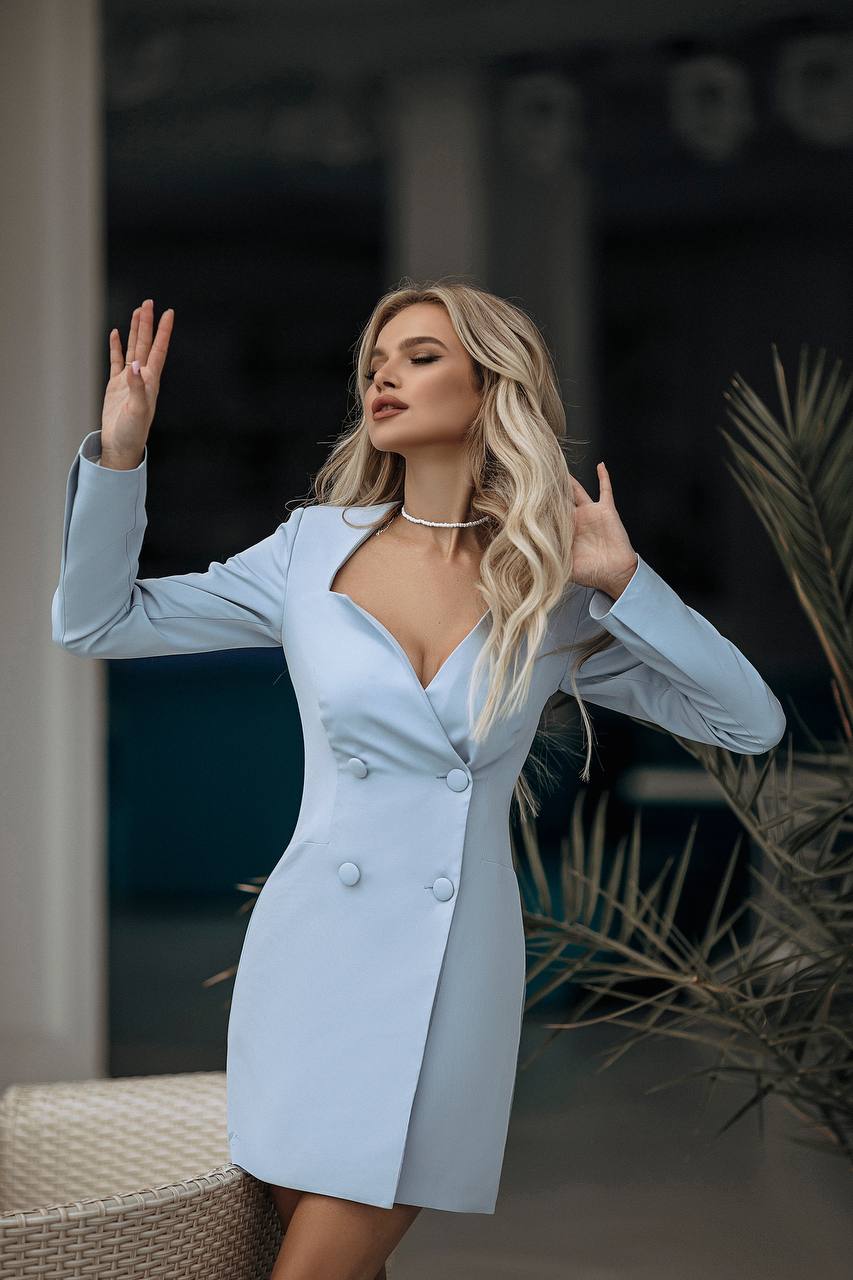 Woman in a light blue dress posing outdoors with plants in the background