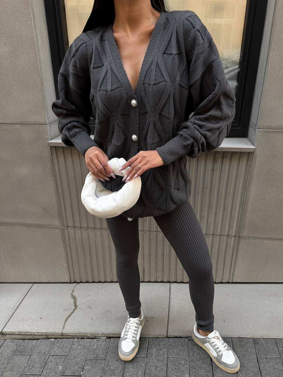 Person wearing a dark gray cardigan and leggings holding a white object against a neutral background