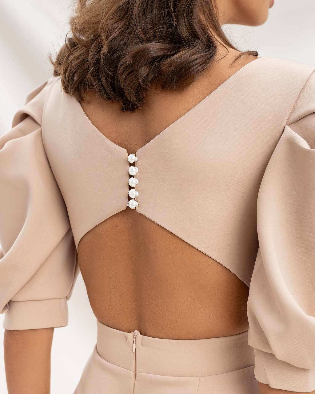 Beige dress with a backless design and pearl buttons on a neutral background