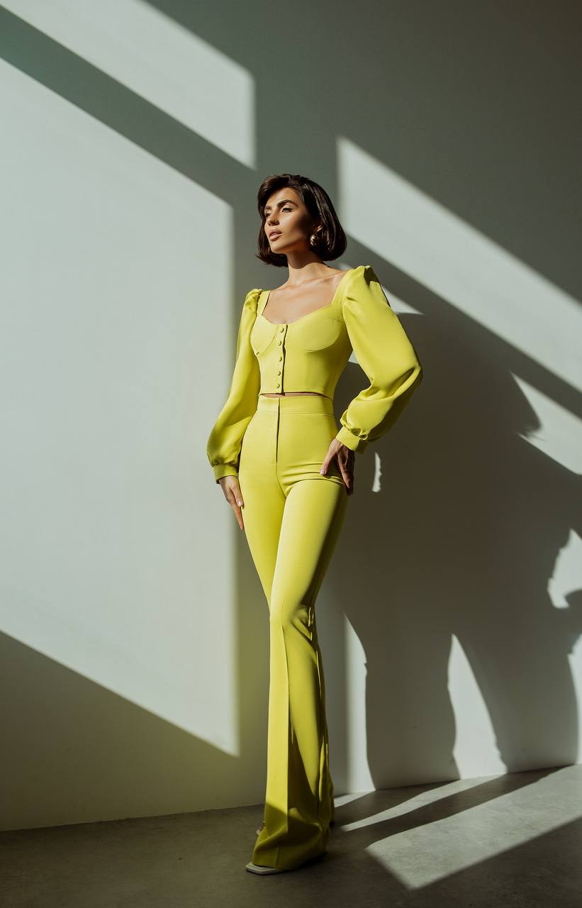 Woman in a bright yellow outfit standing against a wall with light and shadow patterns.