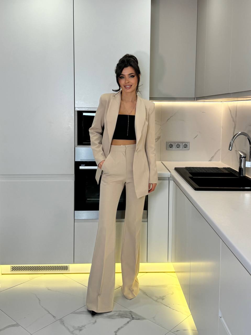 Woman in a beige suit standing in a modern kitchen.