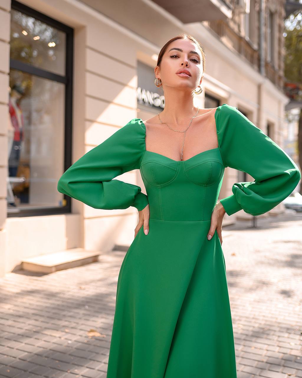 Woman in a green dress standing on a street with buildings in the background