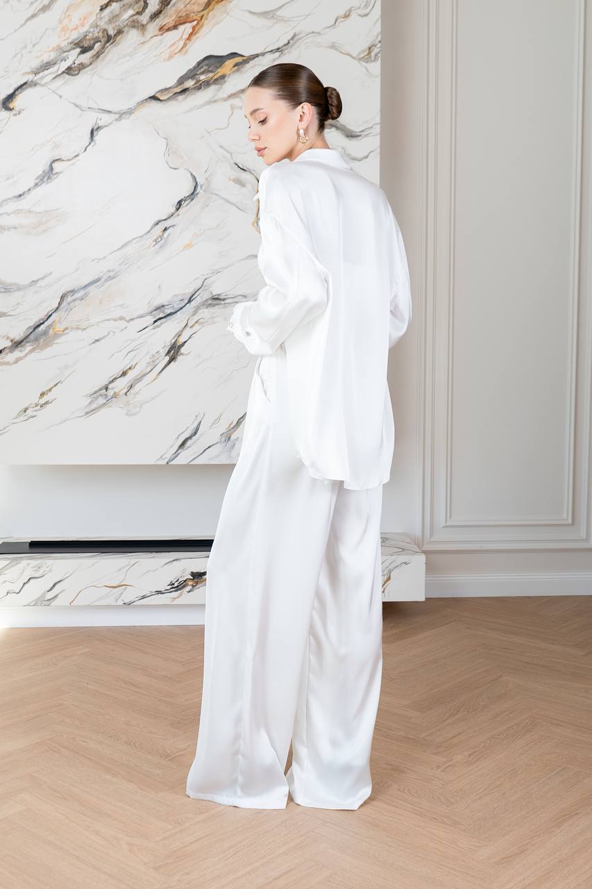 Woman in a white outfit standing in a room with marble wall and wooden floor.