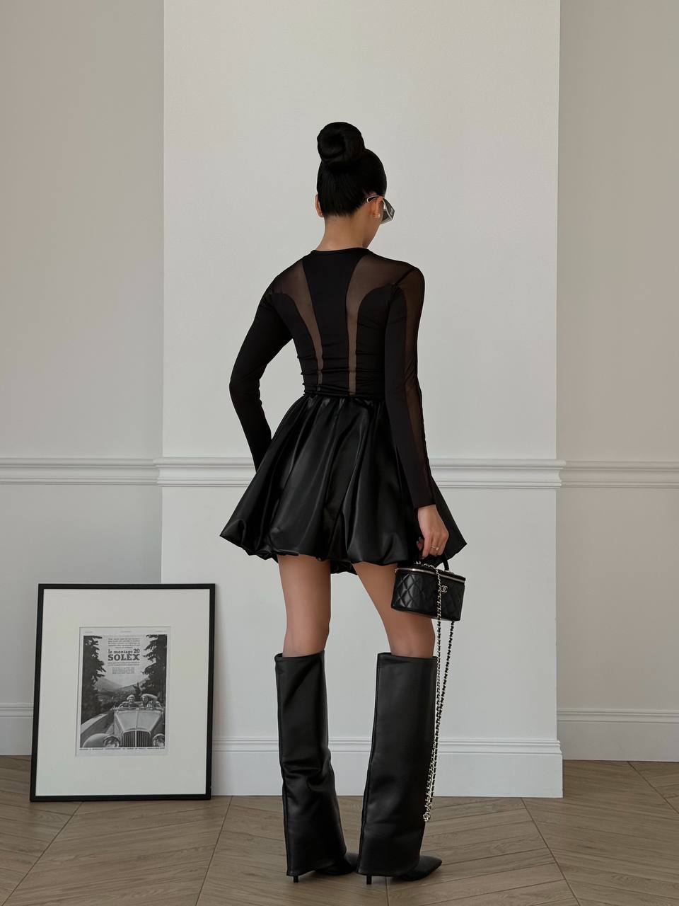 Person wearing a black dress and high boots in a minimalistic room.