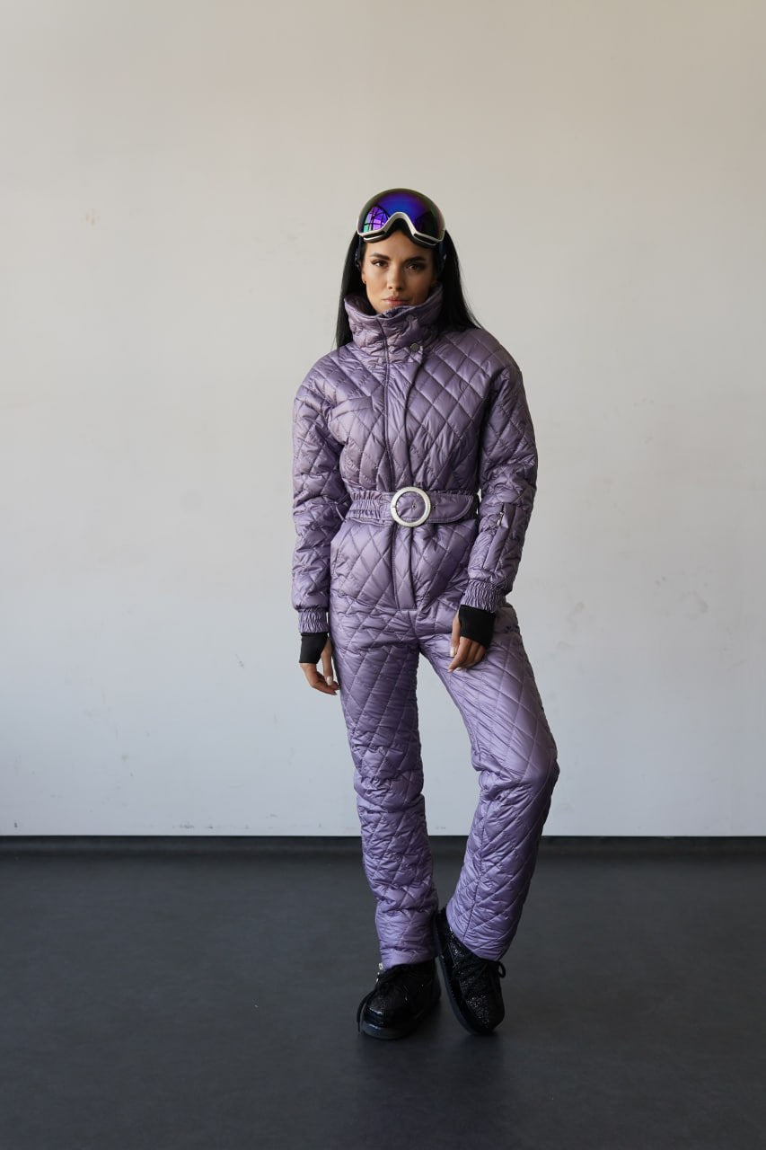 Person wearing a purple quilted snowsuit with goggles on a plain background
