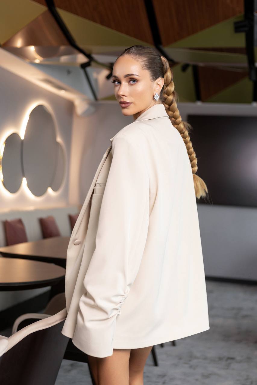 Woman in a beige coat standing in a modern interior setting