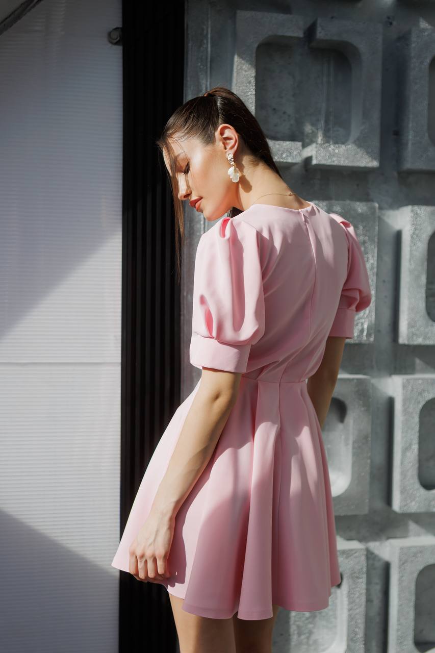 Woman wearing a pink dress against a textured wall.