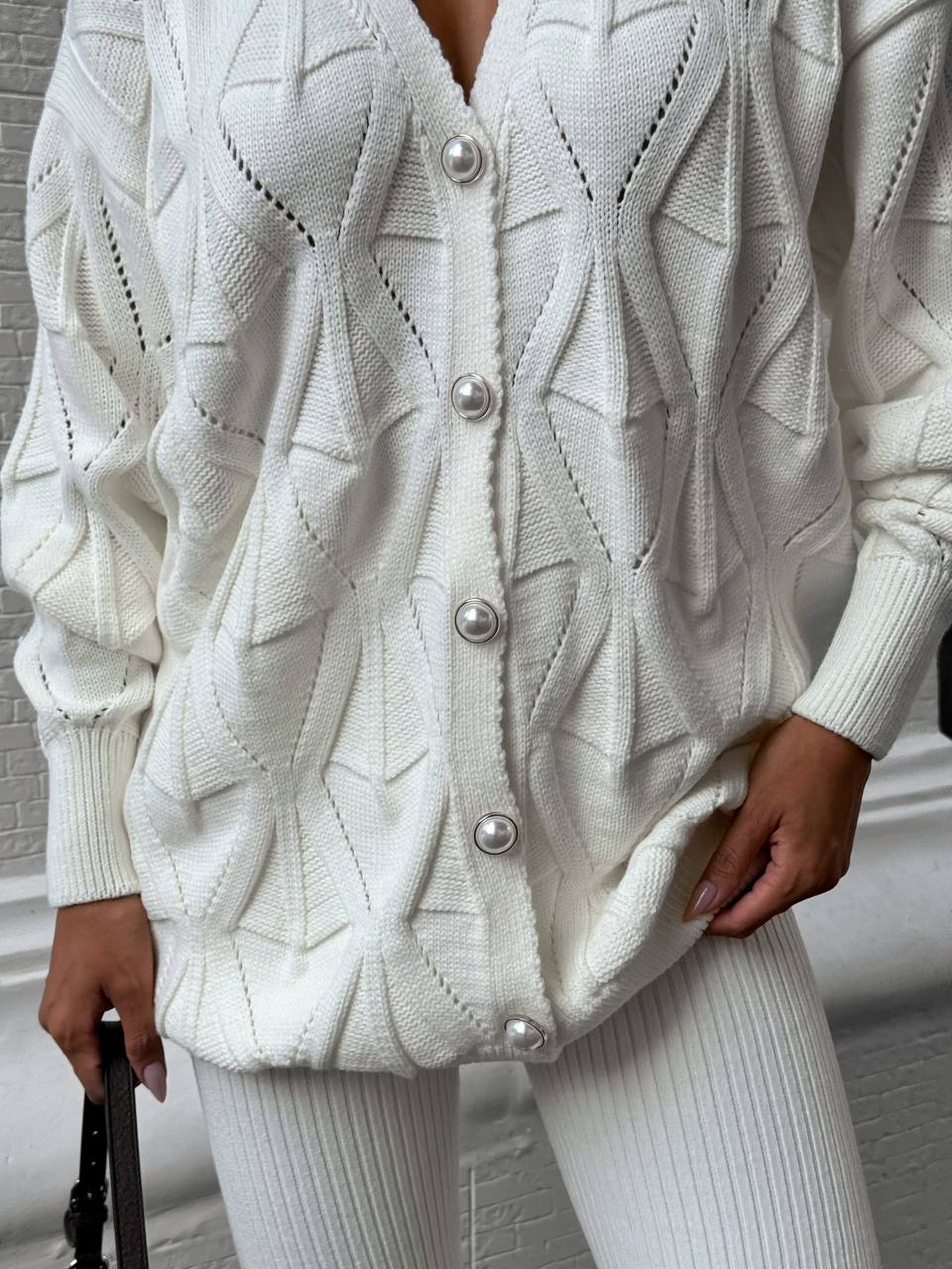 White textured cardigan with pearl buttons worn by a person indoors.