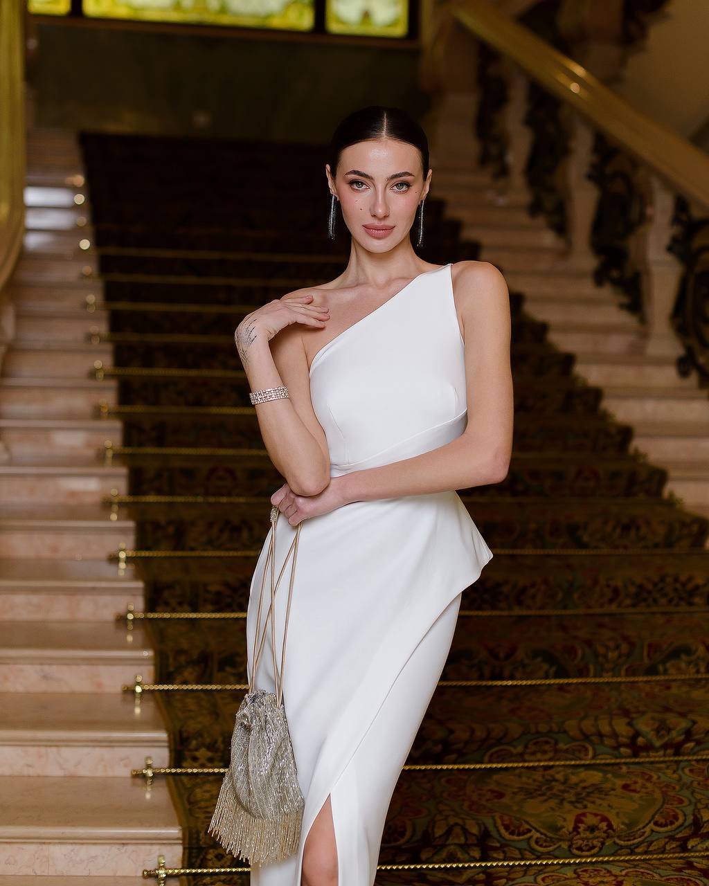 Woman in a white one-shoulder dress standing on a staircase