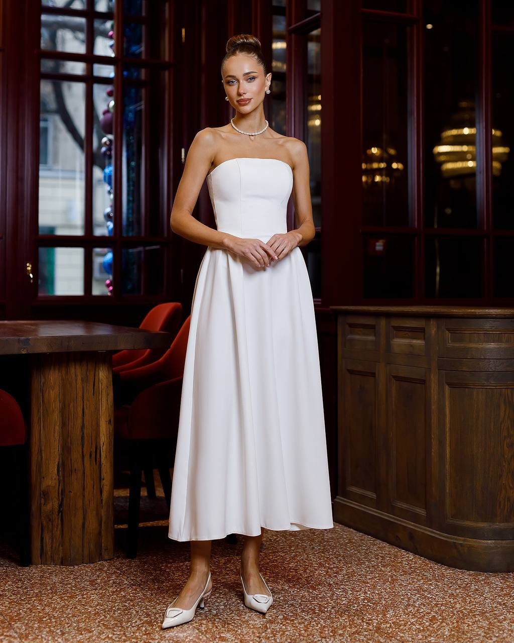 Woman in a white strapless dress standing in an elegant interior setting.