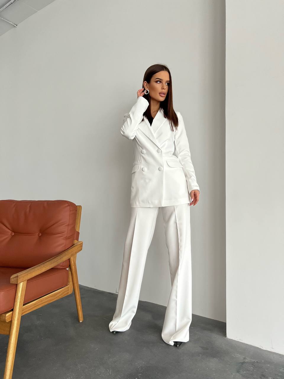 Woman in a white suit standing in a minimalistic room with a red chair.
