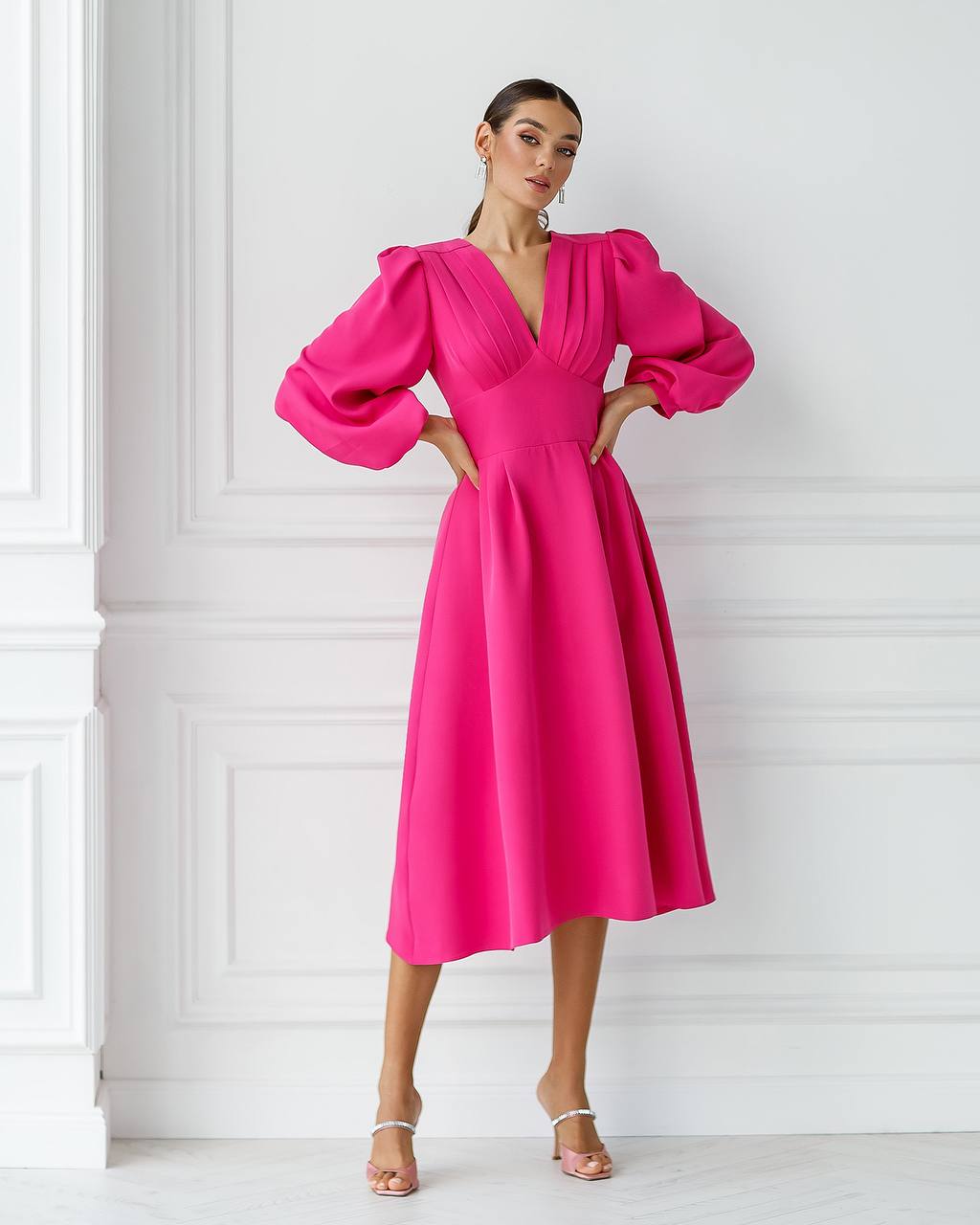 Woman wearing a bright pink dress with puffed sleeves against a white wall.