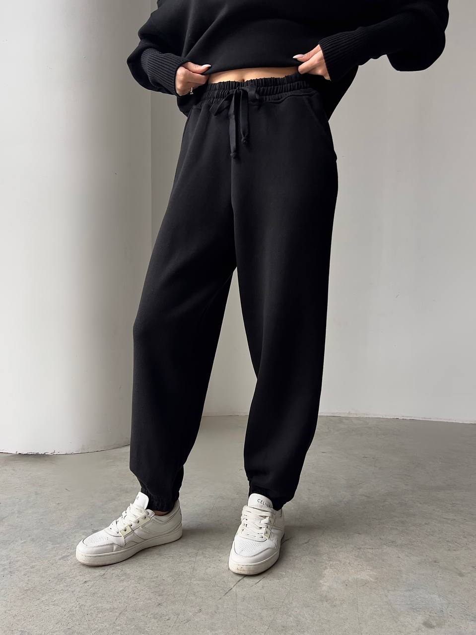 Person wearing black jogger pants and white sneakers on a plain background
