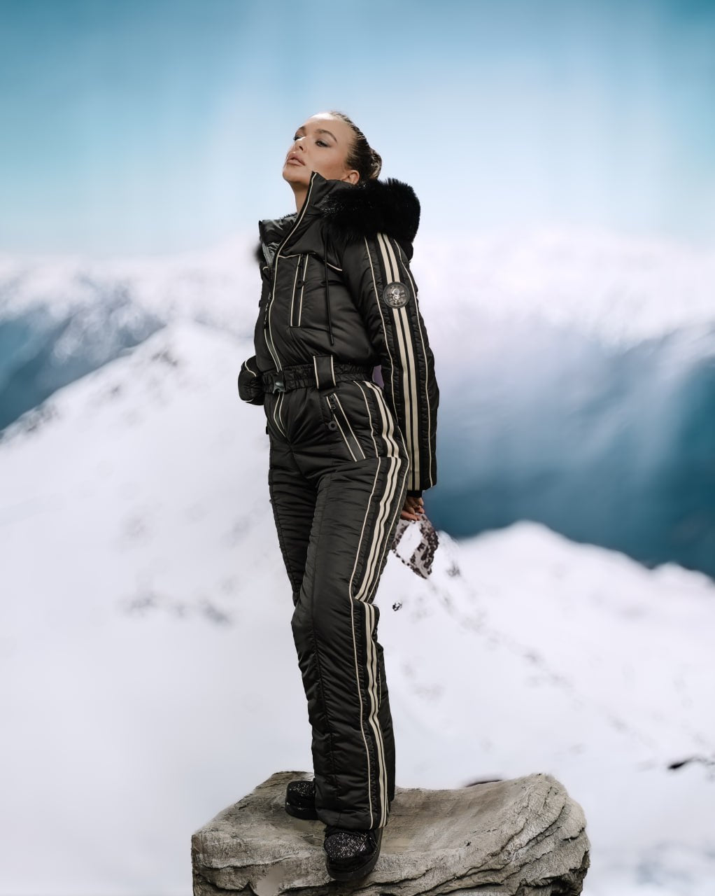 Person wearing a black winter outfit with white stripes on a snowy mountain background