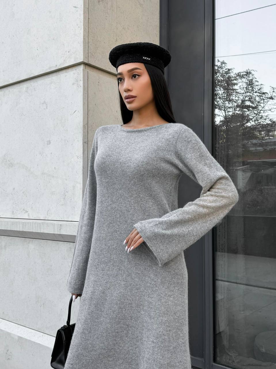 Woman wearing a gray dress and black beret standing against a modern building.