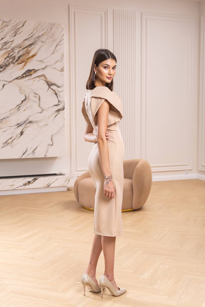 Woman in a beige dress standing in a stylish room with marble wall and furniture.