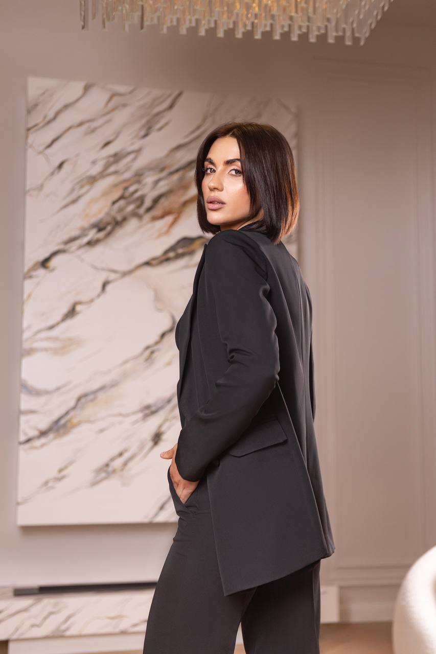 Woman in a black suit standing in a room with a marble wall art piece.