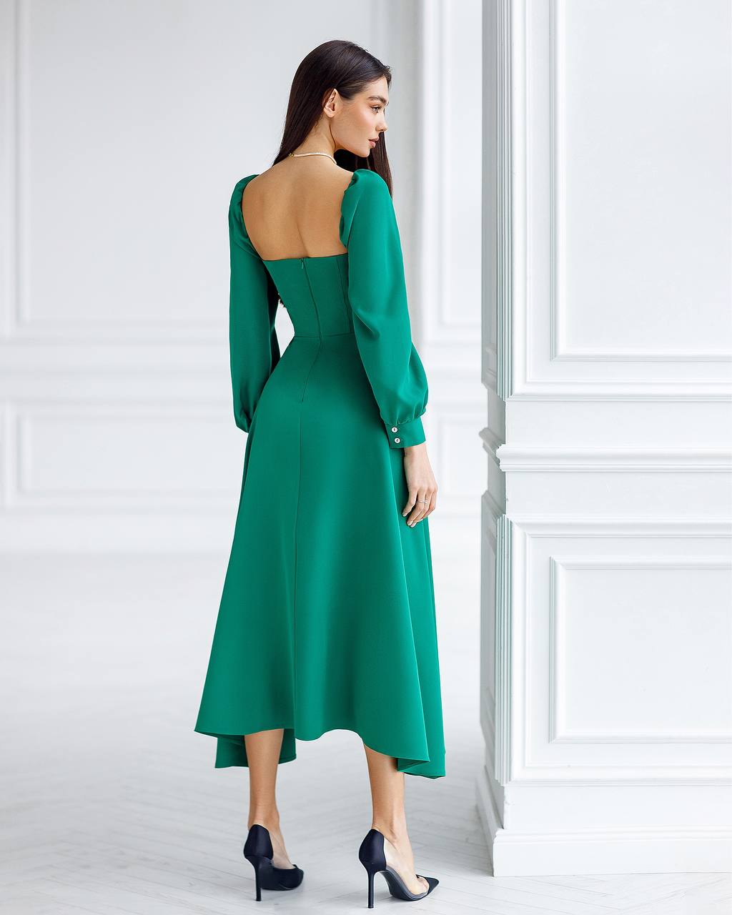 Woman wearing a green dress with a backless design in a white room.