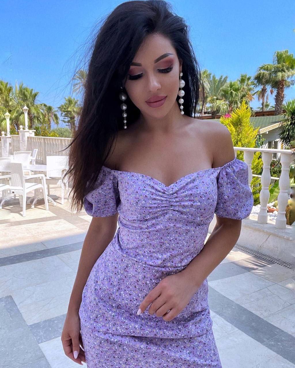 Woman wearing a purple floral dress standing outdoors with palm trees in the background