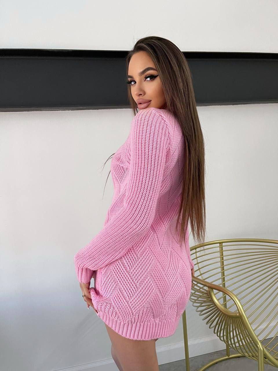 Woman wearing a pink knitted dress standing in a minimalistic room with a chair.