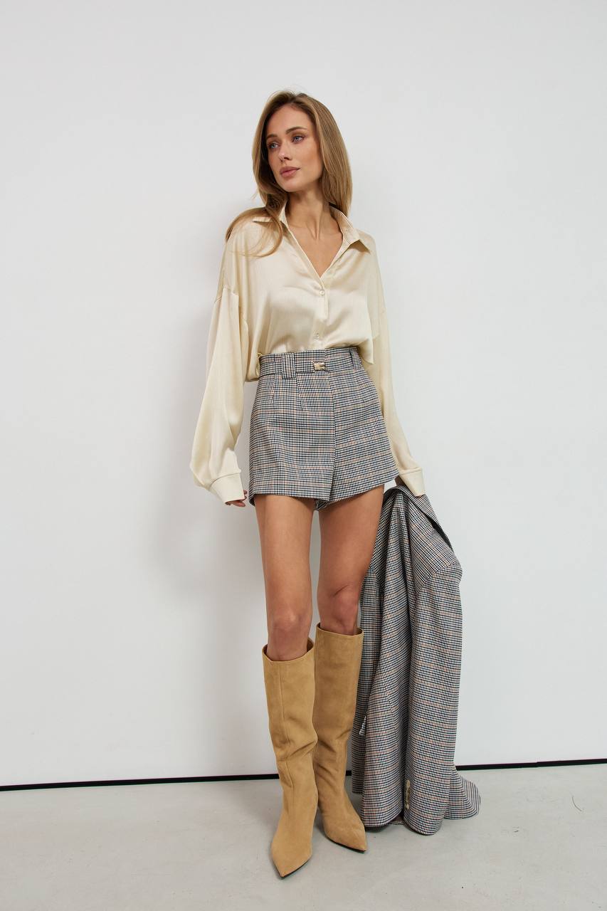 Woman wearing a satin blouse, plaid skirt, and tan knee-high boots against a white background