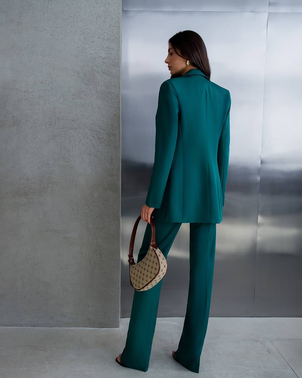 Woman in a teal suit standing against a metallic wall.