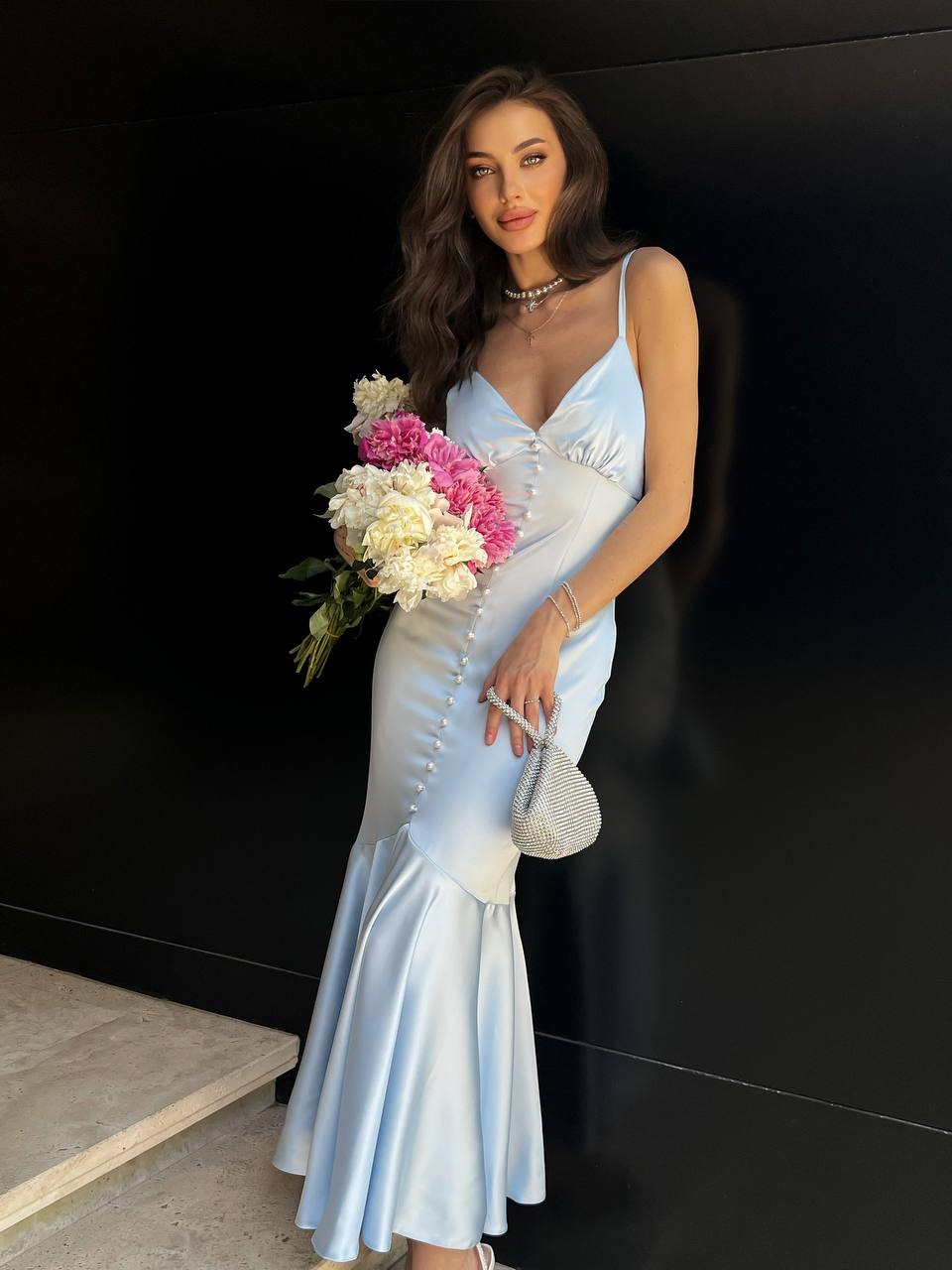 Woman in a light blue dress holding flowers against a black background