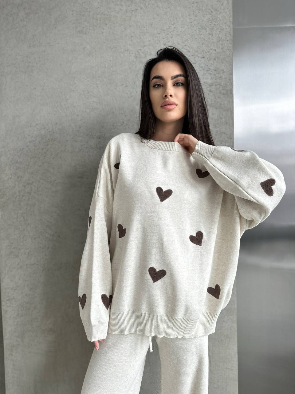 Woman wearing a white sweater with brown heart patterns against a gray background