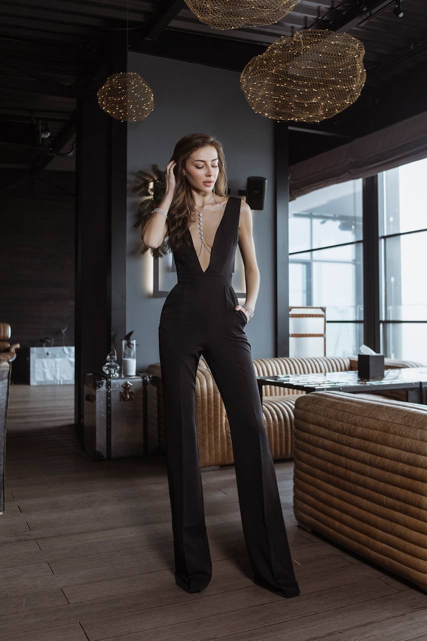 Woman in a black jumpsuit standing in a modern interior setting