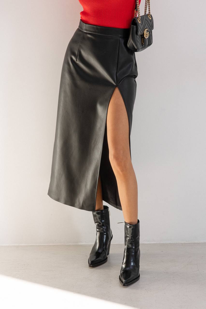 Person wearing a black leather skirt with a high slit, red top, and black boots on a light background.