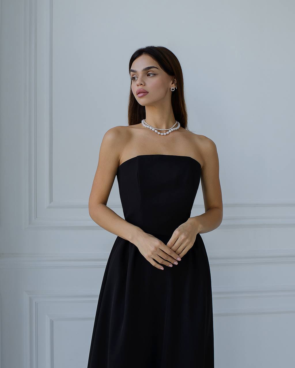 Woman wearing a black strapless dress against a gray wall