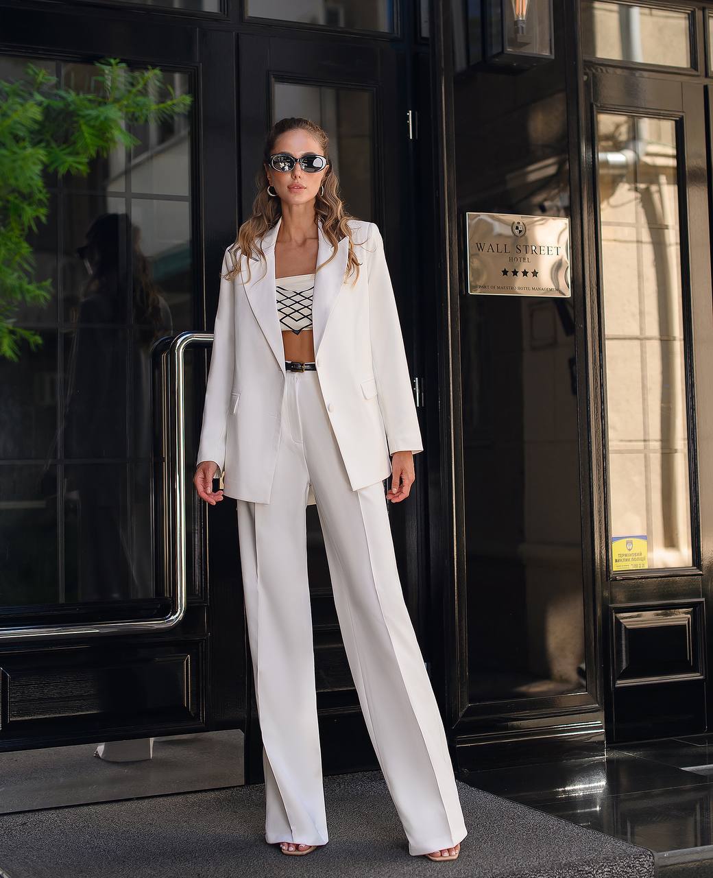 Woman in a white suit standing outside a building with a sign.