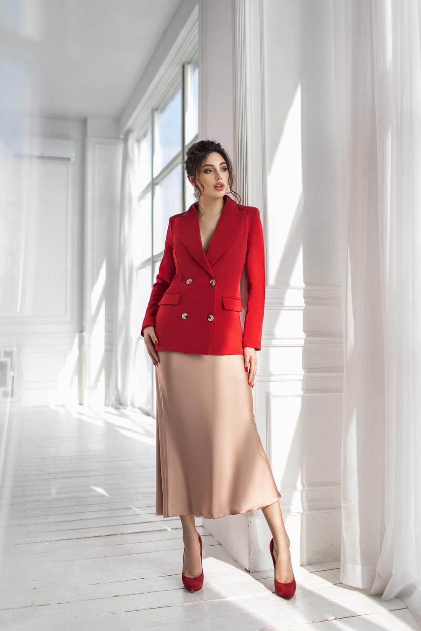 Woman wearing a red blazer and beige skirt in a bright room with white walls and floor.