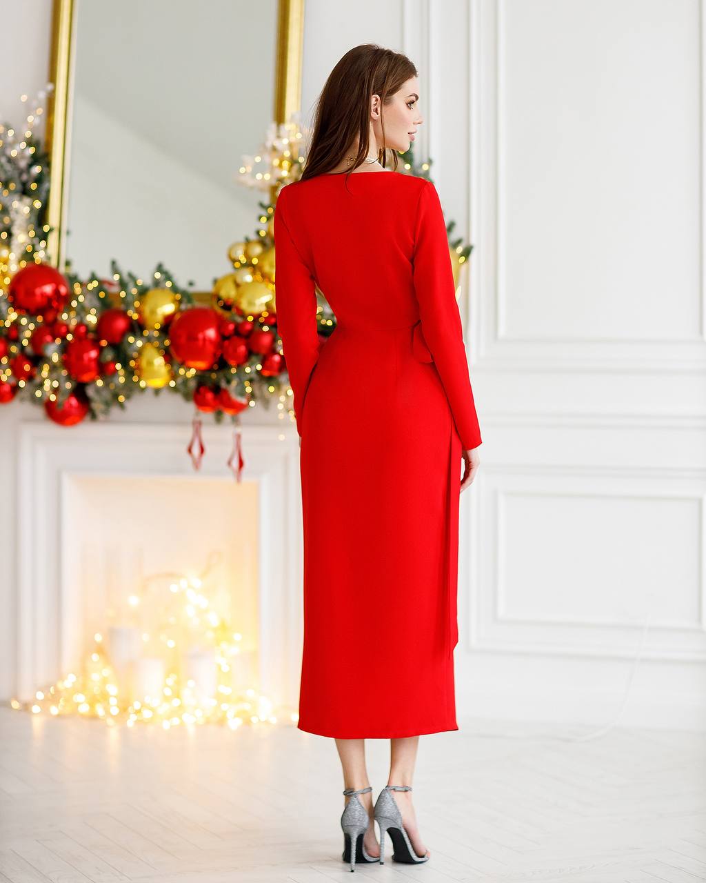Woman in a red dress standing in front of a decorated fireplace with Christmas decorations.