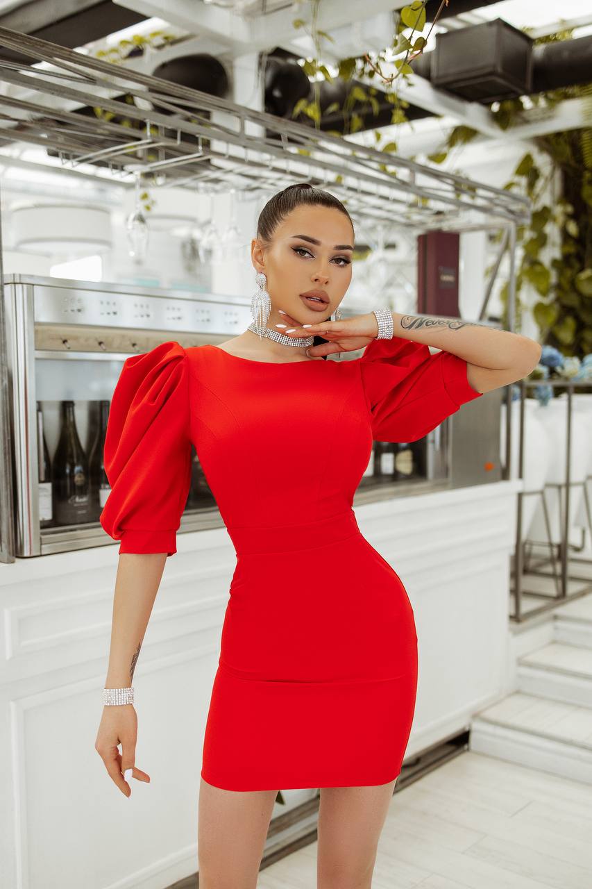 Woman in a red dress posing in an indoor setting with white walls and metal railings.