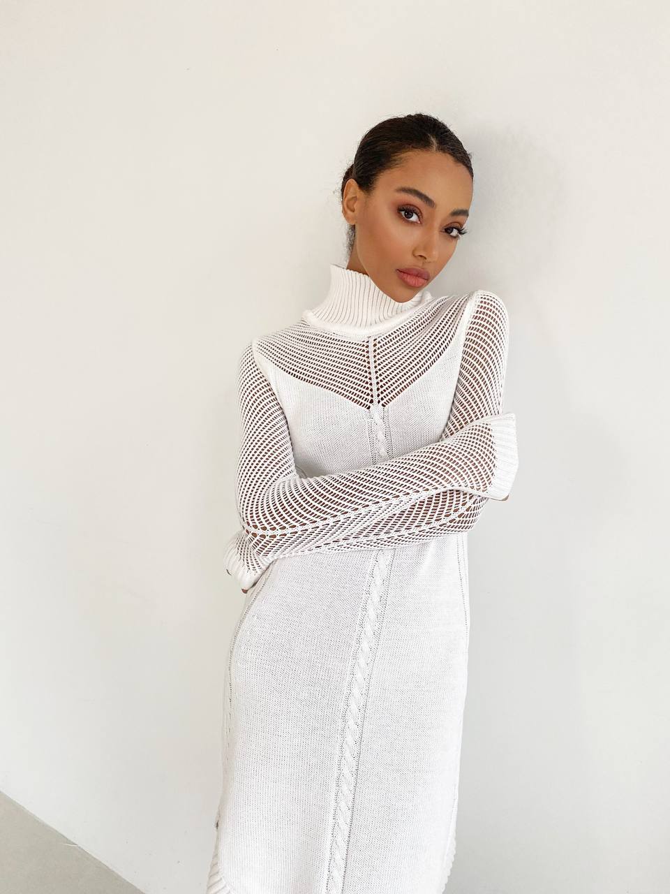 Woman wearing a white dress with a textured shawl against a plain background