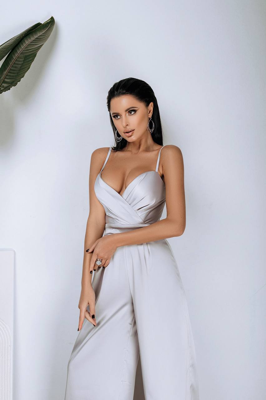Woman in a white jumpsuit posing against a plain background