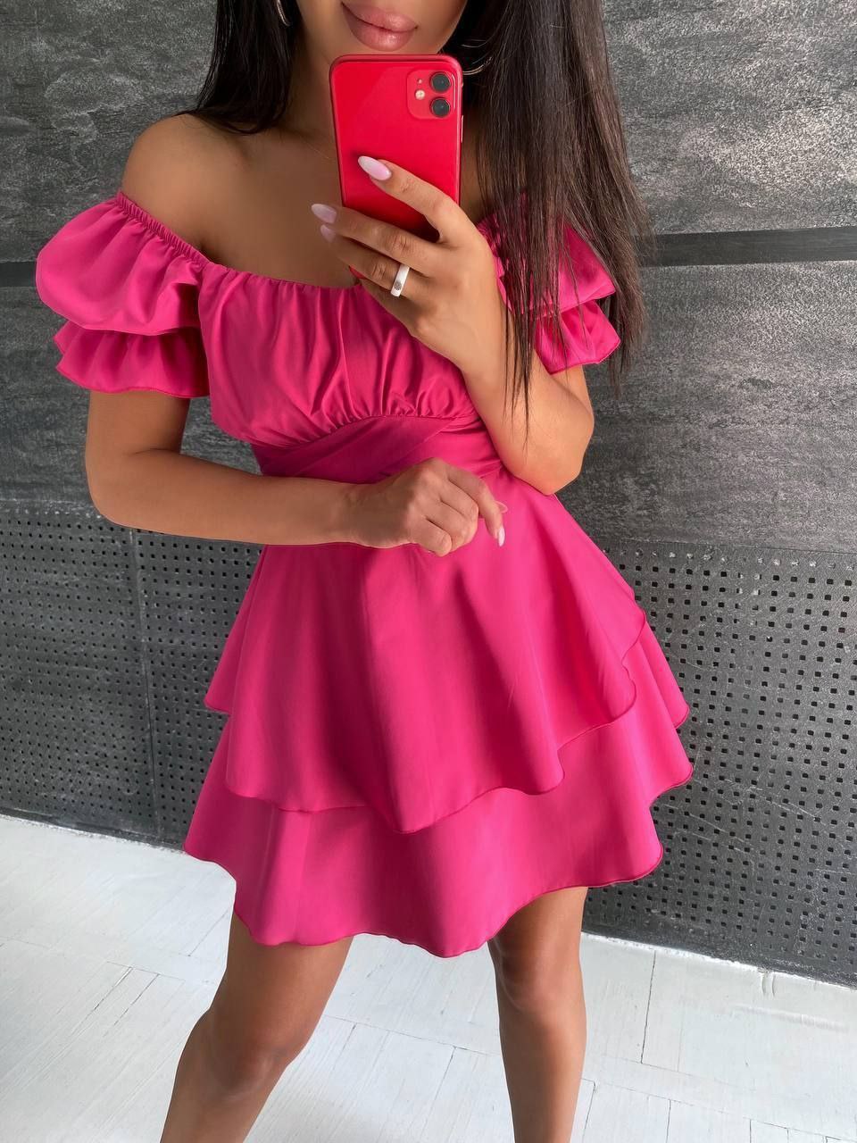 Woman wearing a bright pink off-shoulder dress against a gray wall.
