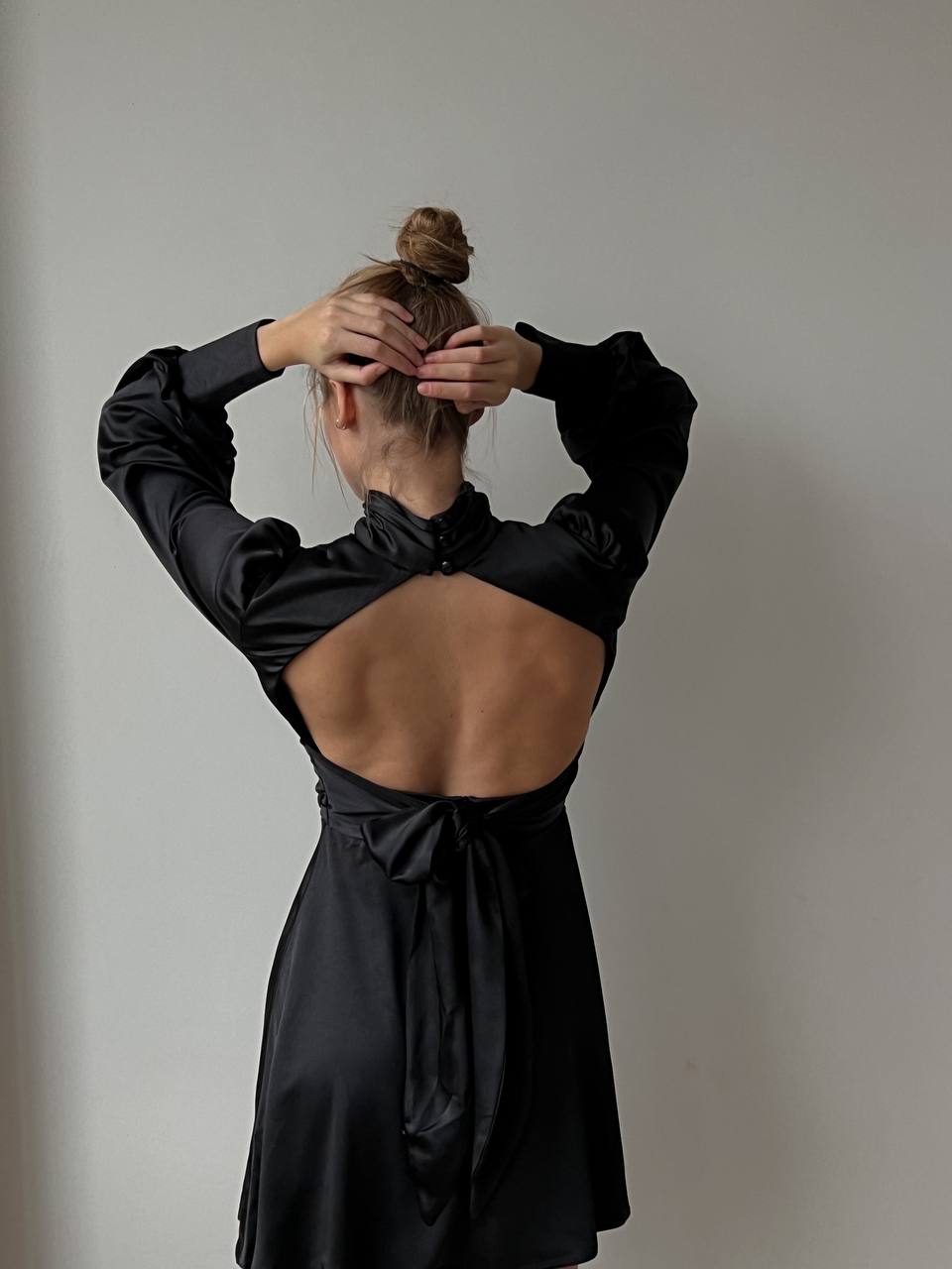 Person wearing a black dress with an open back against a plain background