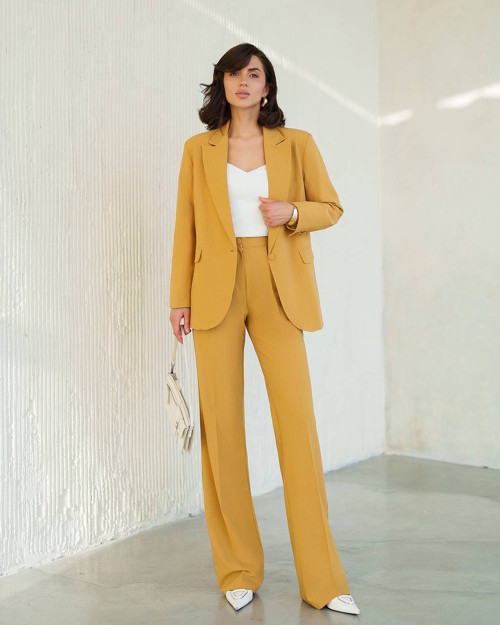 Woman wearing a mustard yellow suit with a white top against a neutral background