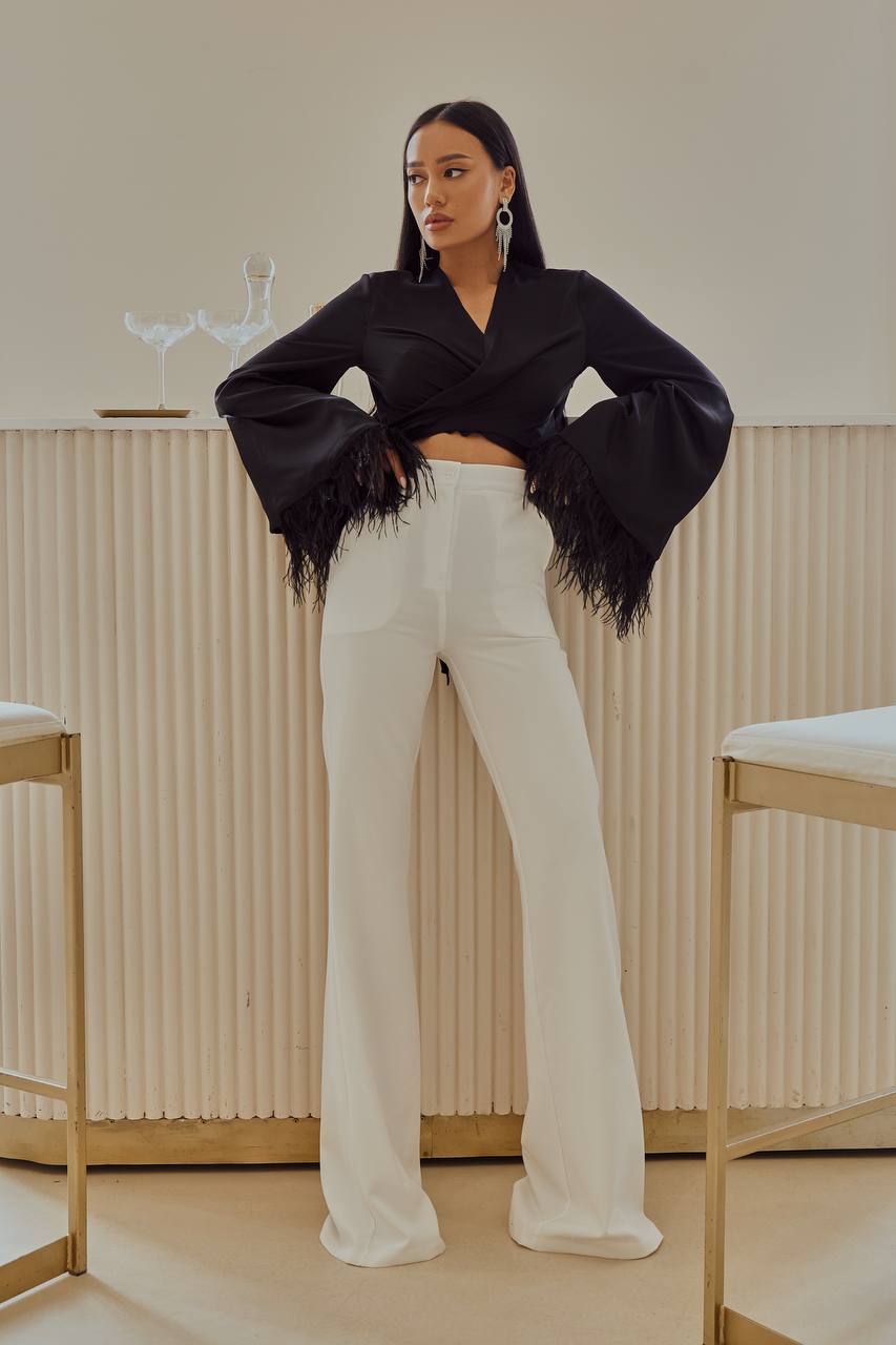 Woman wearing a black fringed jacket and white pants in a minimalistic setting