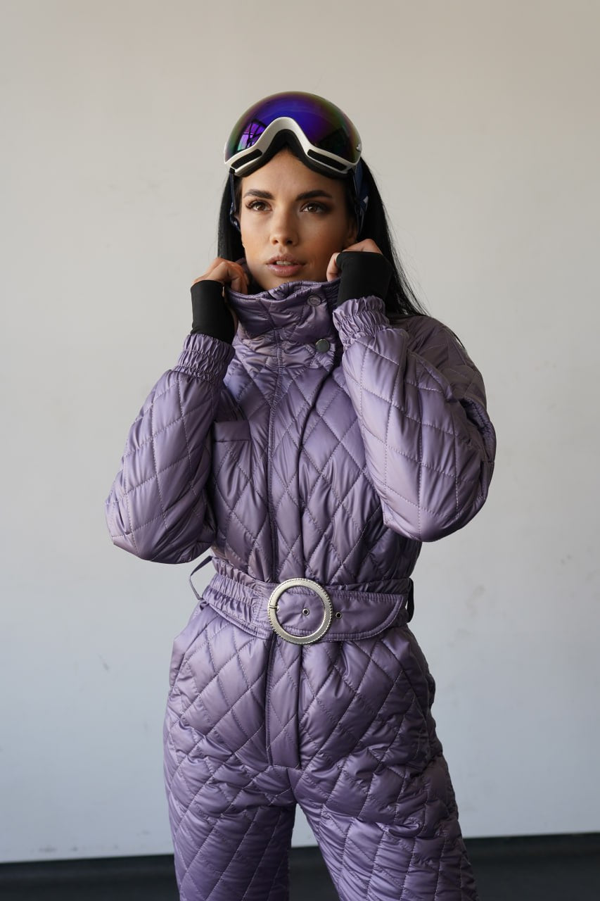 Person wearing a purple quilted snowsuit with goggles on a plain background