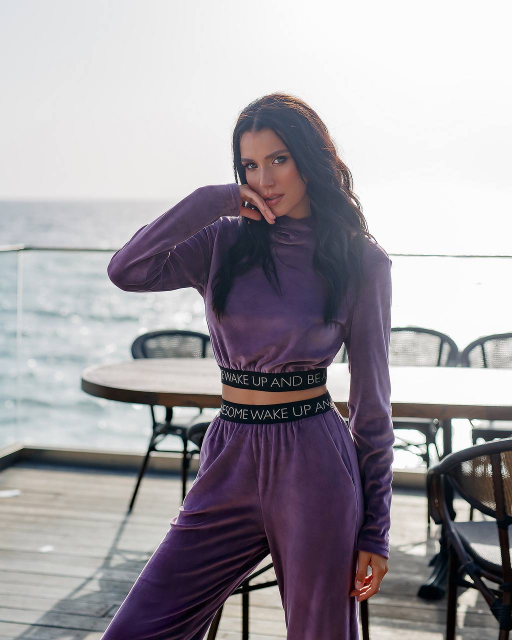 Woman in a purple outfit standing on a rooftop with tables and chairs in the background.