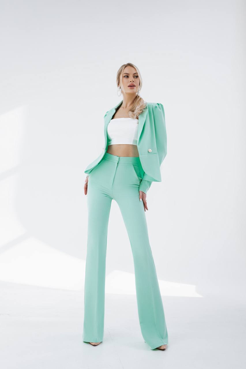 Woman wearing a mint green suit with a white top on a white background